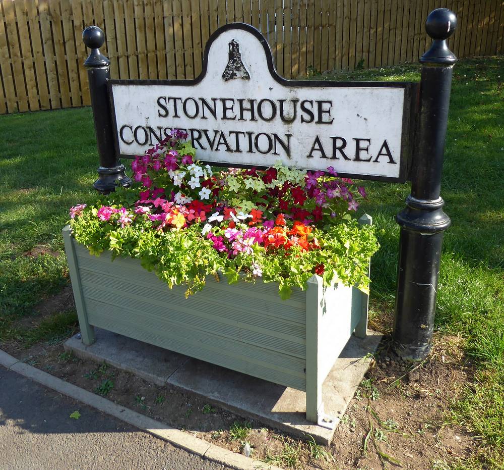 Conservation Area sign and flower planter opposite the church at the junction of Lawrie Street and Crow Road.
